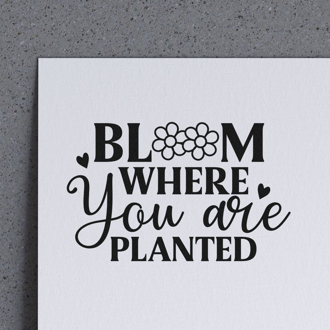 Black stamp and seal design reading Bloom where you are planted with flower icons and hearts on white paper.