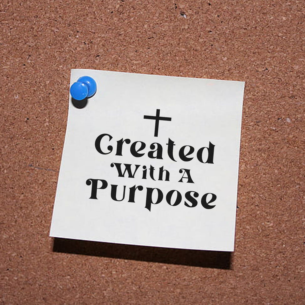White stamp-seal design reading Created With A Purpose in black with a cross, pinned by blue tacks on a corkboard.