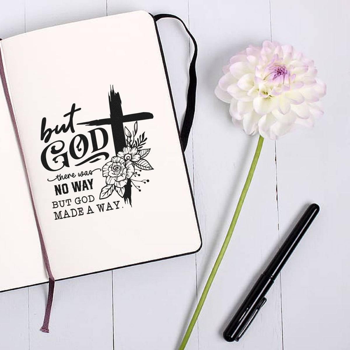 Christian stamp and seal product on cream notebook, black floral cross design, beside white flower and black pen.