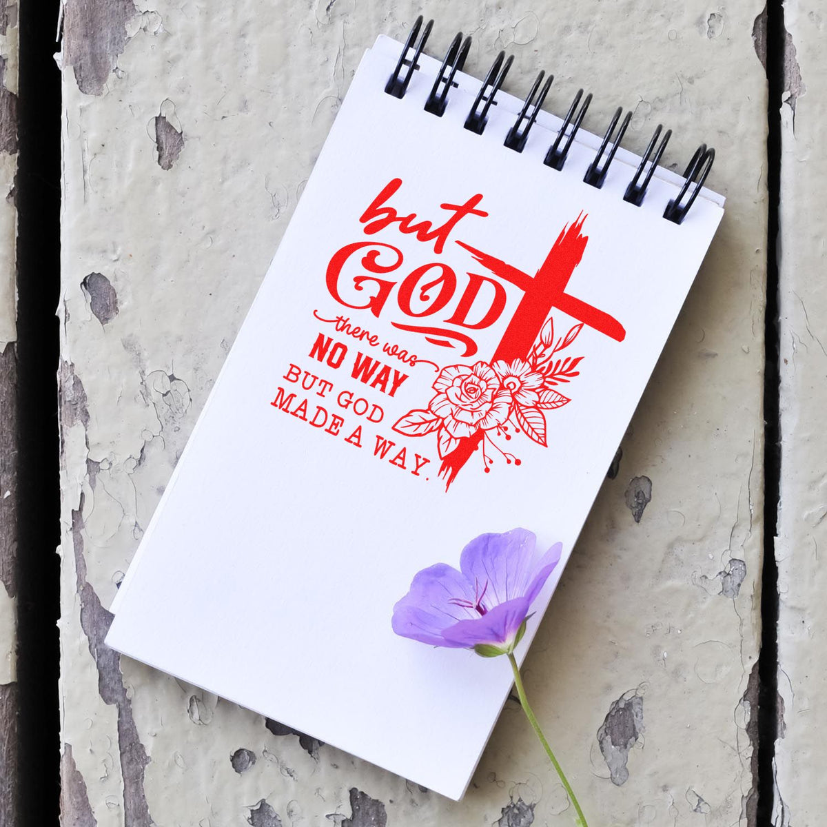 Red Christian stamp and seal design on a white spiral notebook, featuring a cross, floral accents, and a purple flower.