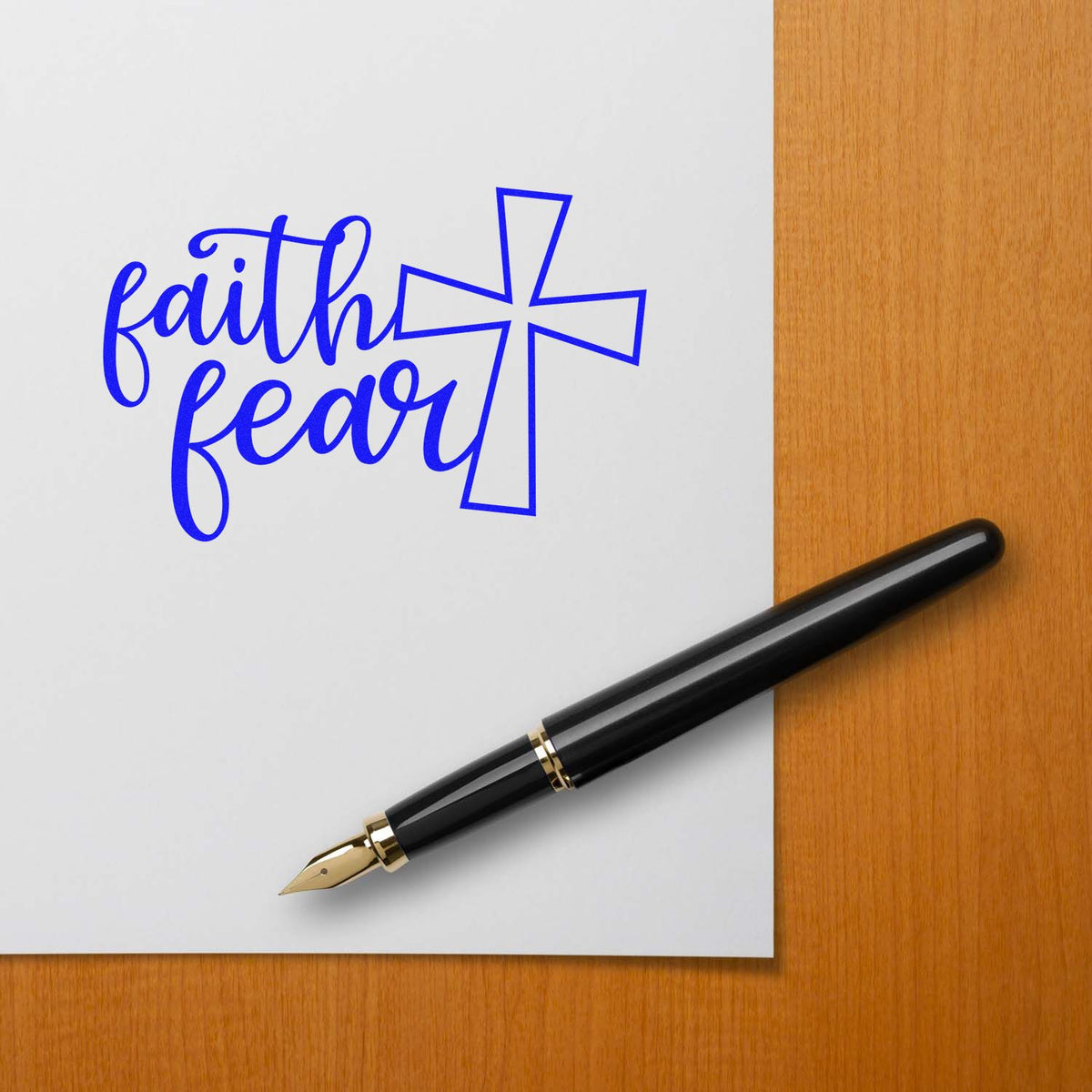 Blue faith over fear cross stamp and seal design on white paper, with black fountain pen on a wood desk.