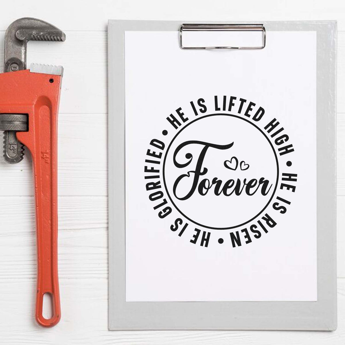 Orange pipe wrench beside clipboard with black He Is Lifted High, He Is Risen stamp seal design and hearts.