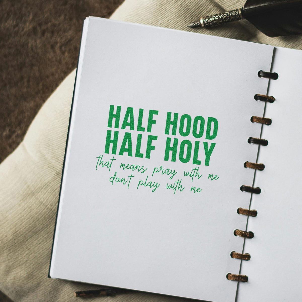 Green stamp-and-seal on white notebook page reads HALF HOOD HALF HOLY, with handwritten script and brown disc binding.