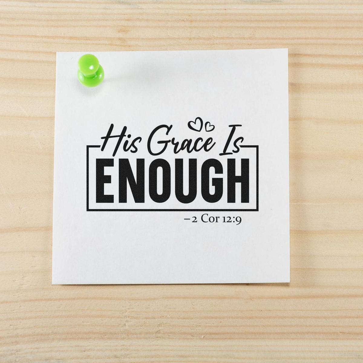 Black faith stamp and seal design on white paper, reading His Grace Is ENOUGH, with green pushpin on wood background.