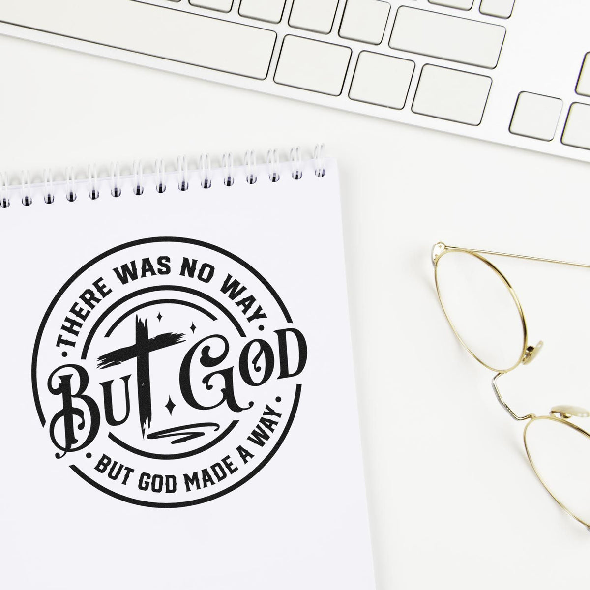 Black custom stamp seal on a white notepad reads There was no way but God made a way, beside gold glasses and a white keyboard.