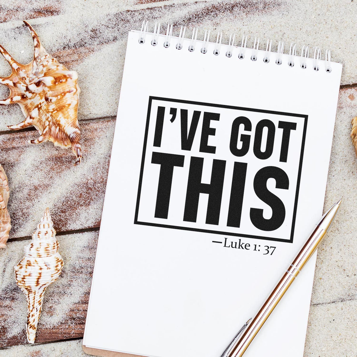 Black stamp and seal design on white spiral notebook, reading IVE GOT THIS  Luke 1:37, with seashells and gold pen.