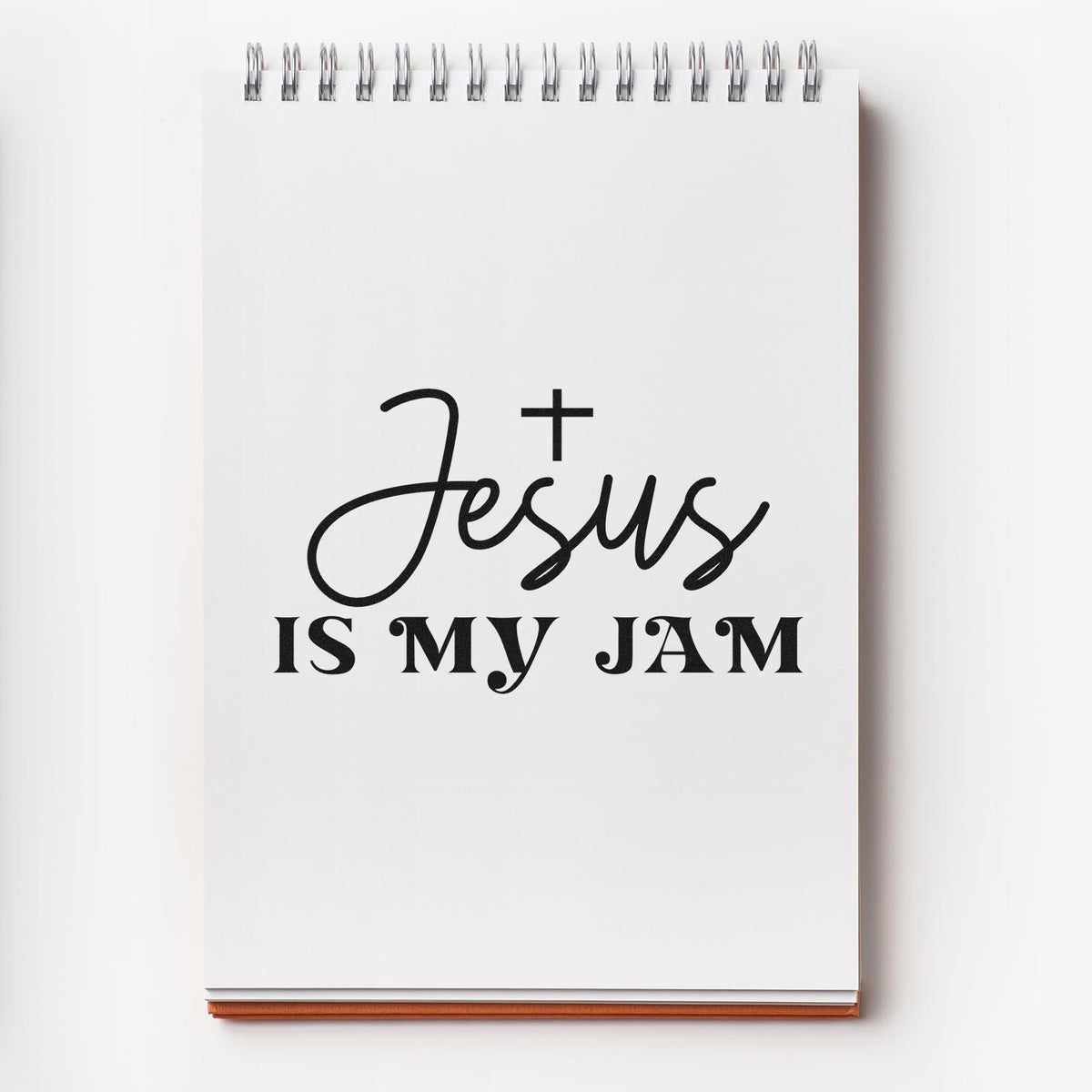 White spiral notebook stamp and seal design with black Jesus is my Jam lettering, silver coils, and white cover on a clean background.