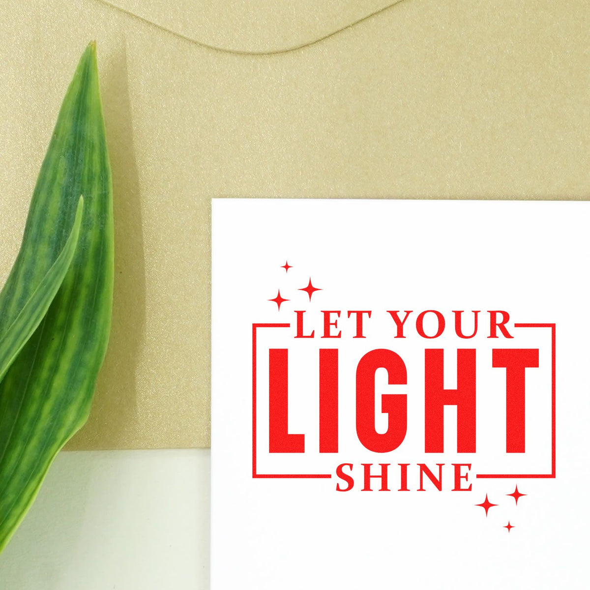 Red Let Your Light Shine stamp and seal design on white card with sparkles, beside a green leaf on beige background.