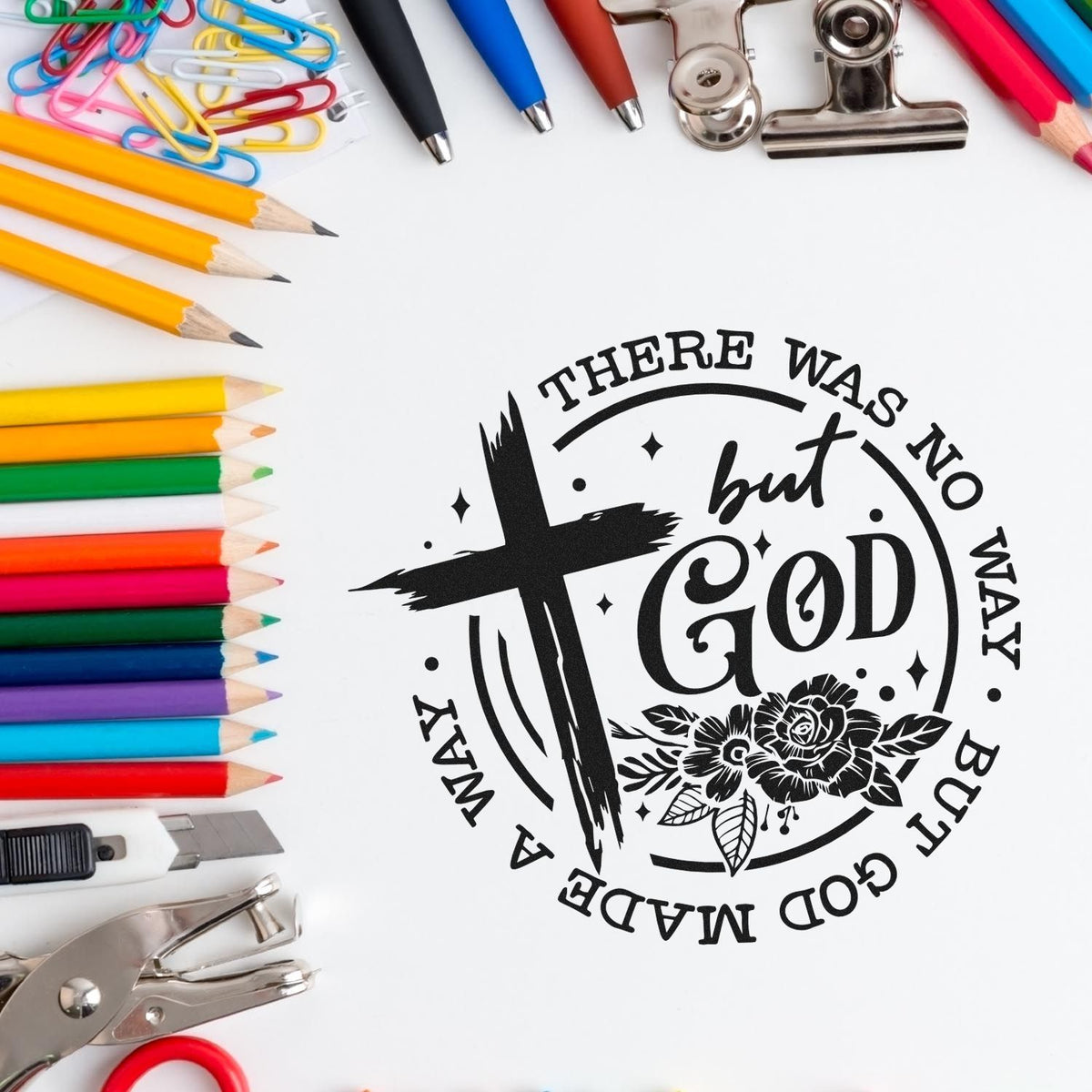 Black faith stamp seal with cross and flowers, surrounded by colorful pencils, pens, clips, and office supplies.