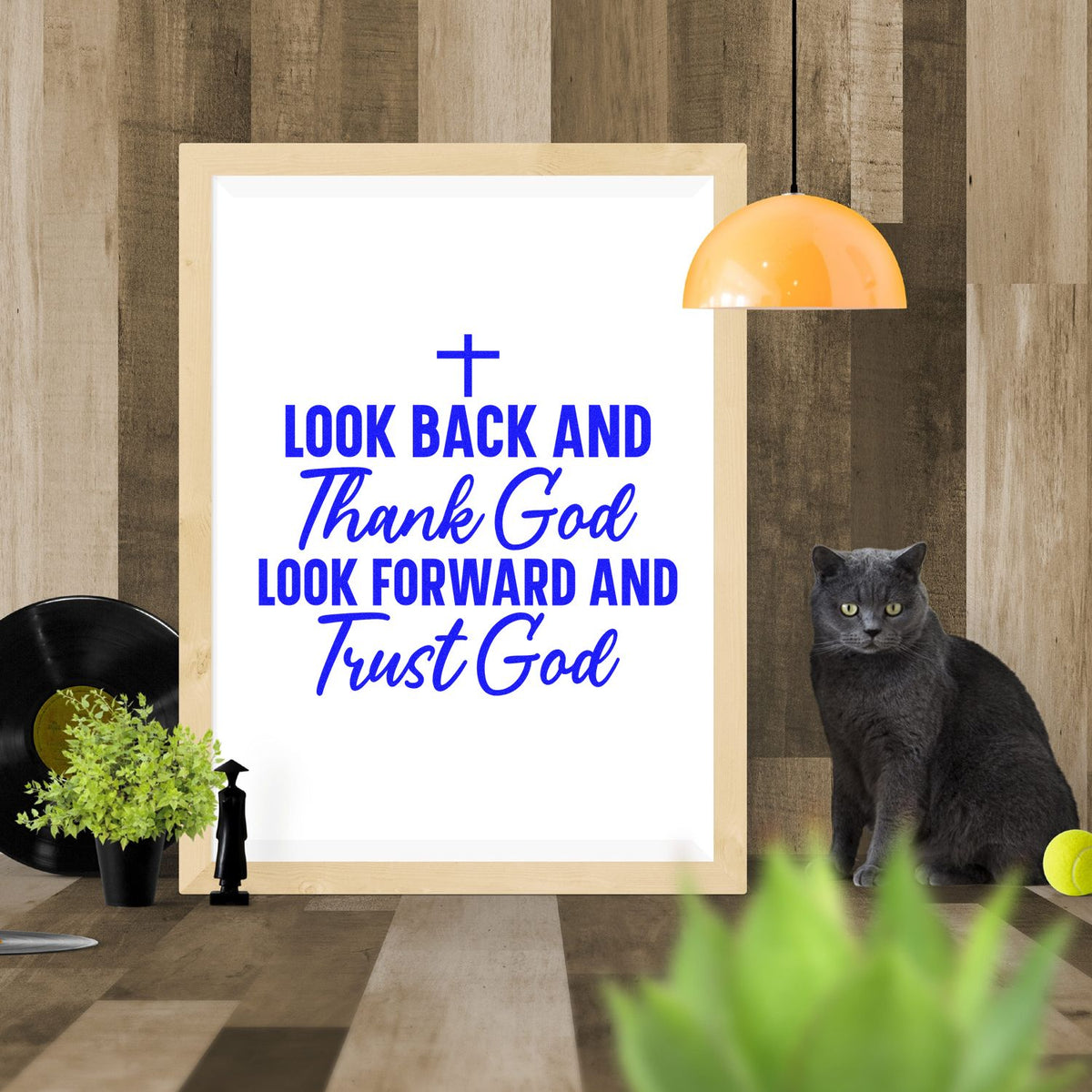 Blue stamp and seal design with religious quote in a light wood frame, white background, gray cat, and orange pendant lamp.