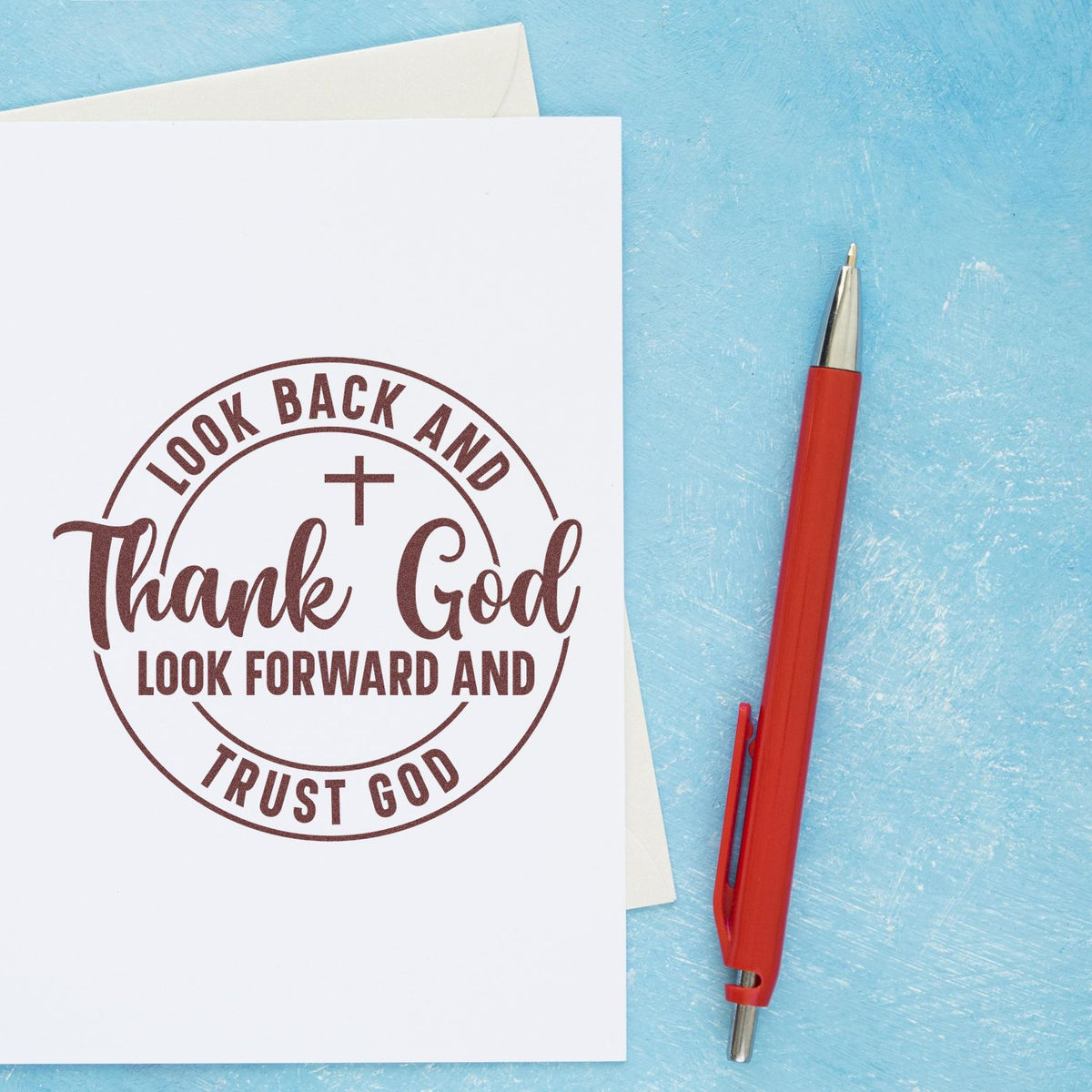 Brown circular stamp seal on white card reads Look Back and Thank God, Look Forward and Trust God; red pen on blue backdrop.