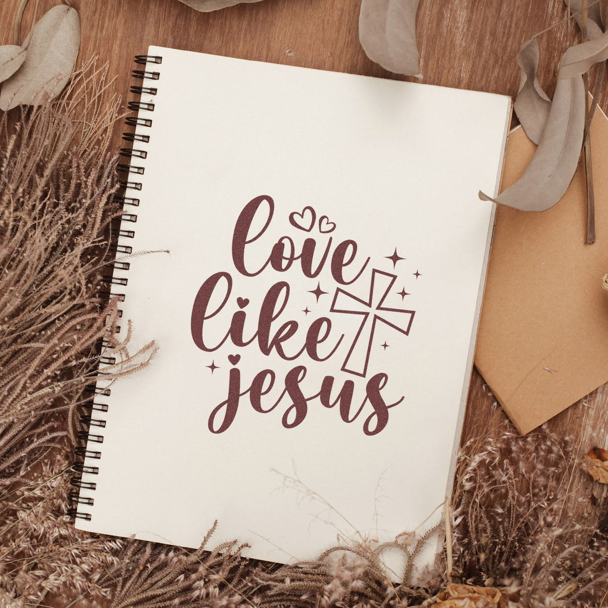 Maroon Christian stamp/seal design reading love like Jesus with cross and hearts on a cream spiral notebook.