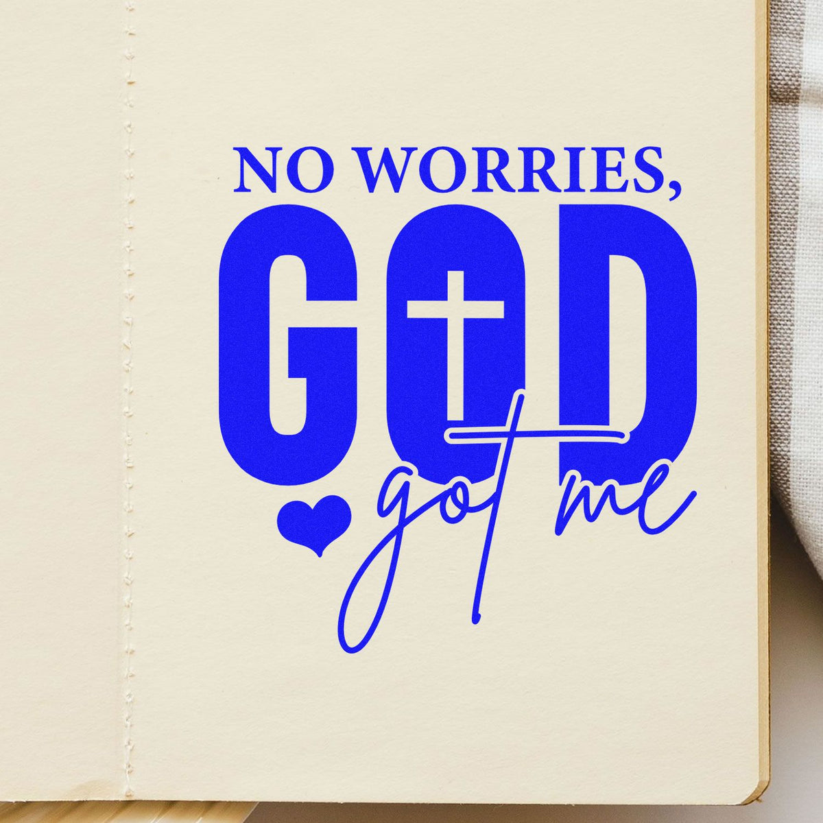 Blue custom stamp on cream paper reading No Worries, God got me with a heart icon and bold cross lettering.
