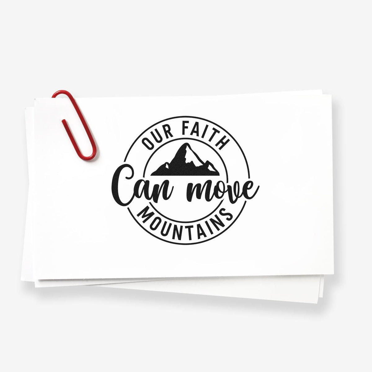 Black circular faith stamp seal on white cards, reading Our Faith Can Move Mountains with mountain icon and red paperclip.