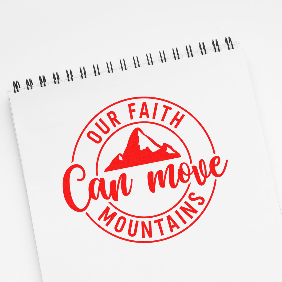 Red circular faith stamp seal on white spiral notebook, with mountain graphic and Can move mountains text.