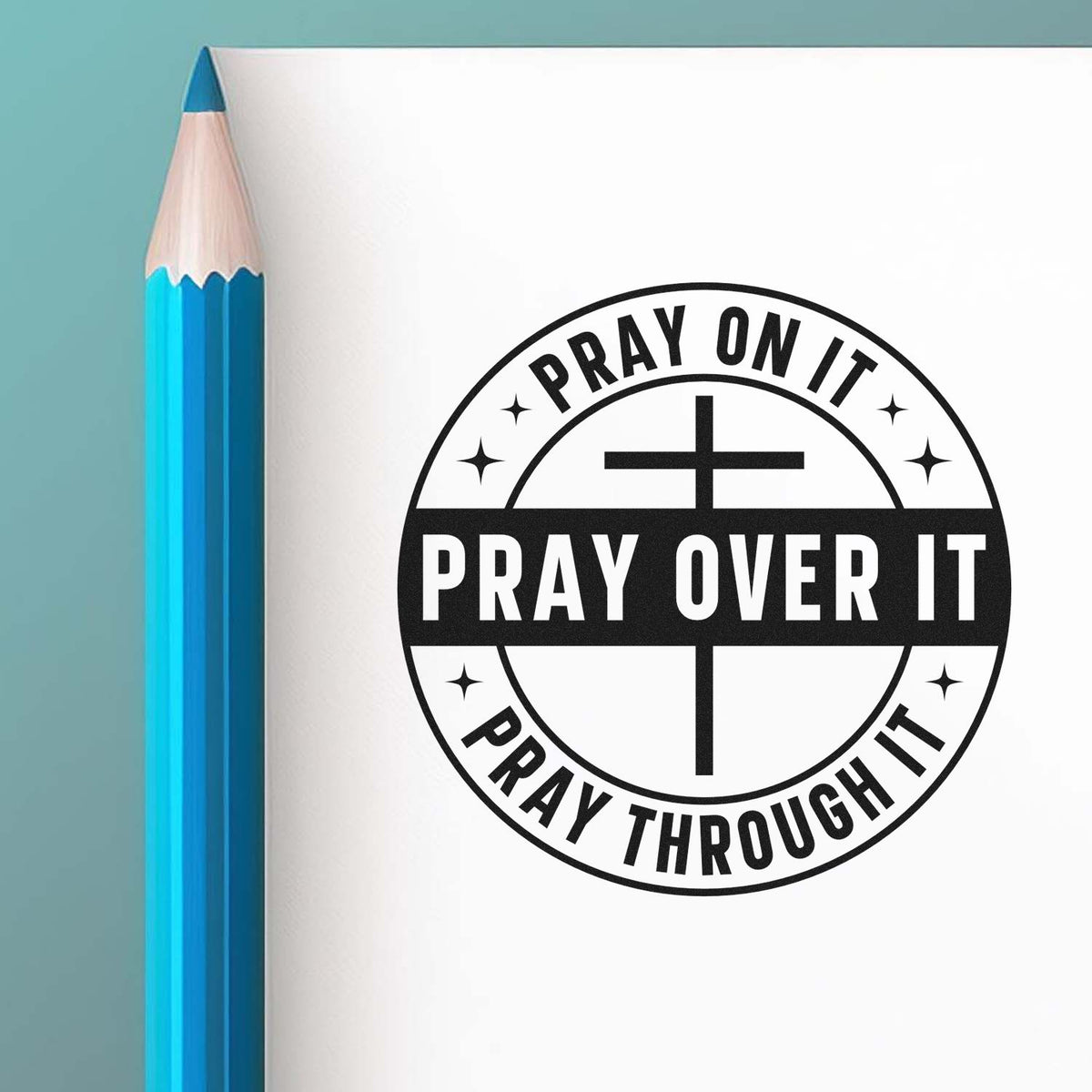 Blue pencil beside white page with black circular prayer stamp seal and cross reading Pray on it, pray over it, pray through it.