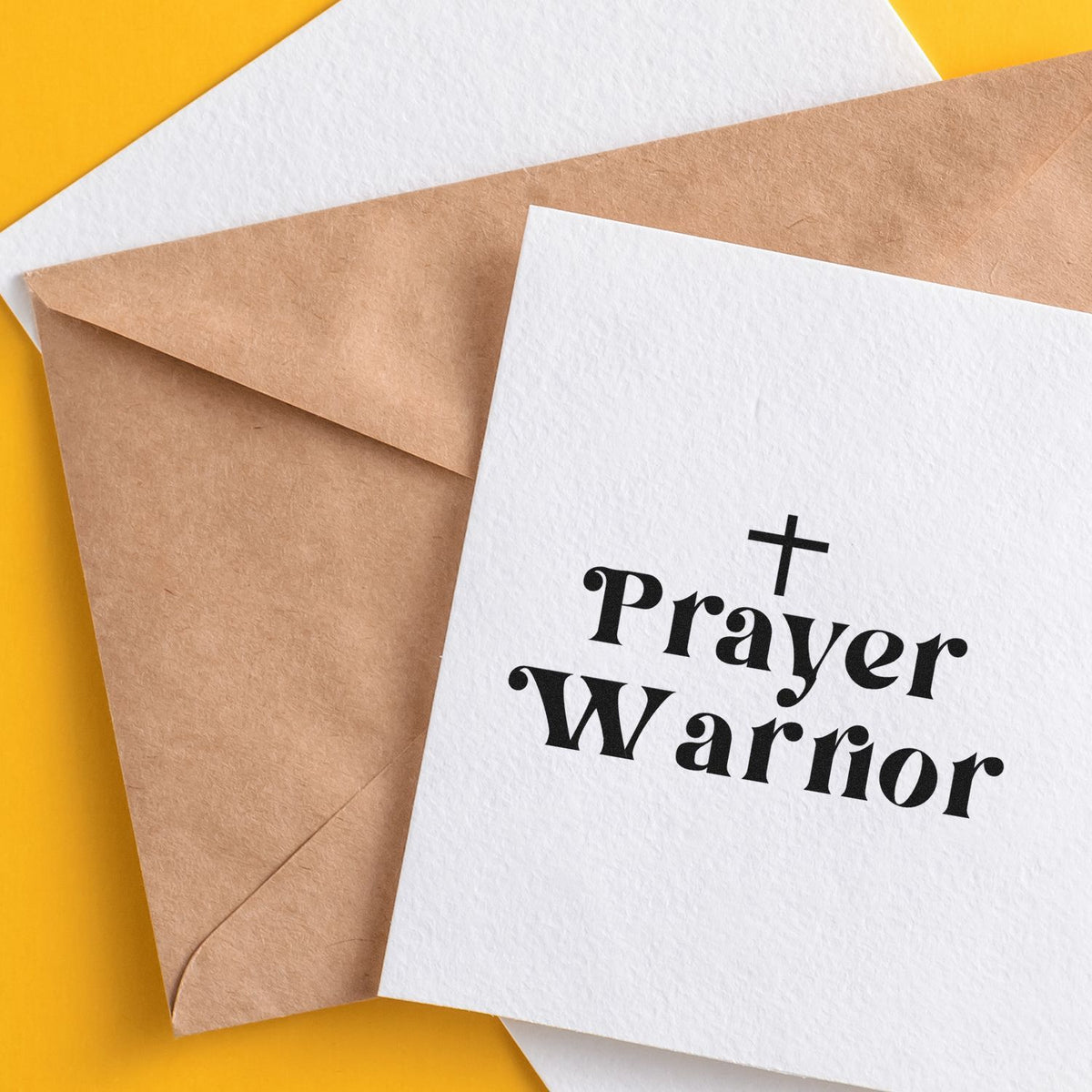 Prayer Warrior stamp and seal card with black cross on white paper, layered over a brown kraft envelope on bright yellow.