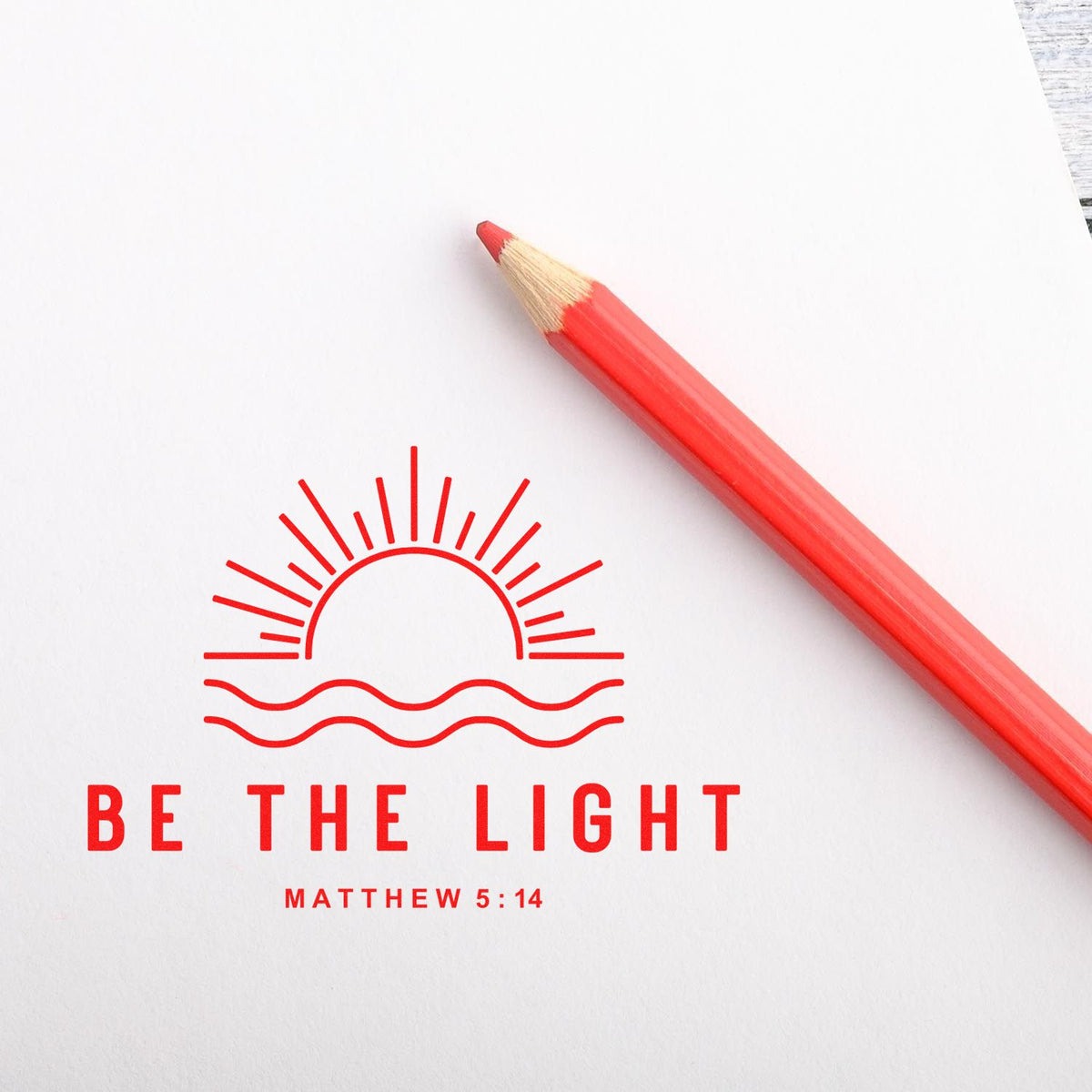 Red stamp seal design with sunburst and waves beside a red pencil on white paper, reading Be the Light Matthew 5:14