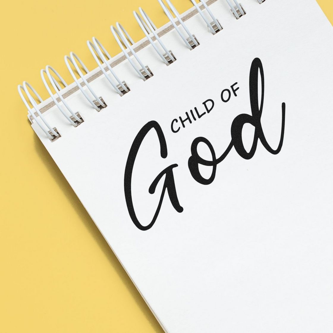 Black Child of God stamp/seal in cursive on a white spiral notebook, with a yellow background.