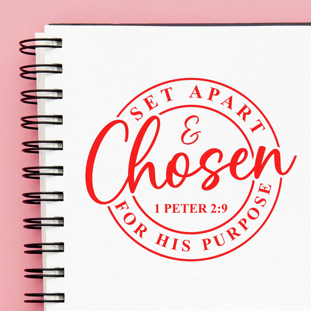 Red circular stamp seal reading Chosen for His Purpose on a white spiral notebook over a pink background.