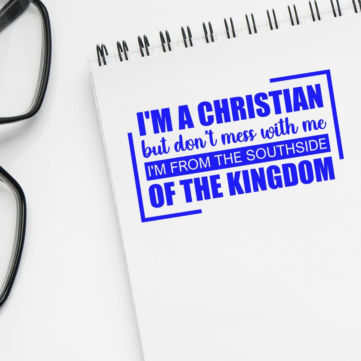 Blue custom stamp seal reading Im a Christian..., on a white spiral notebook beside black eyeglasses.
