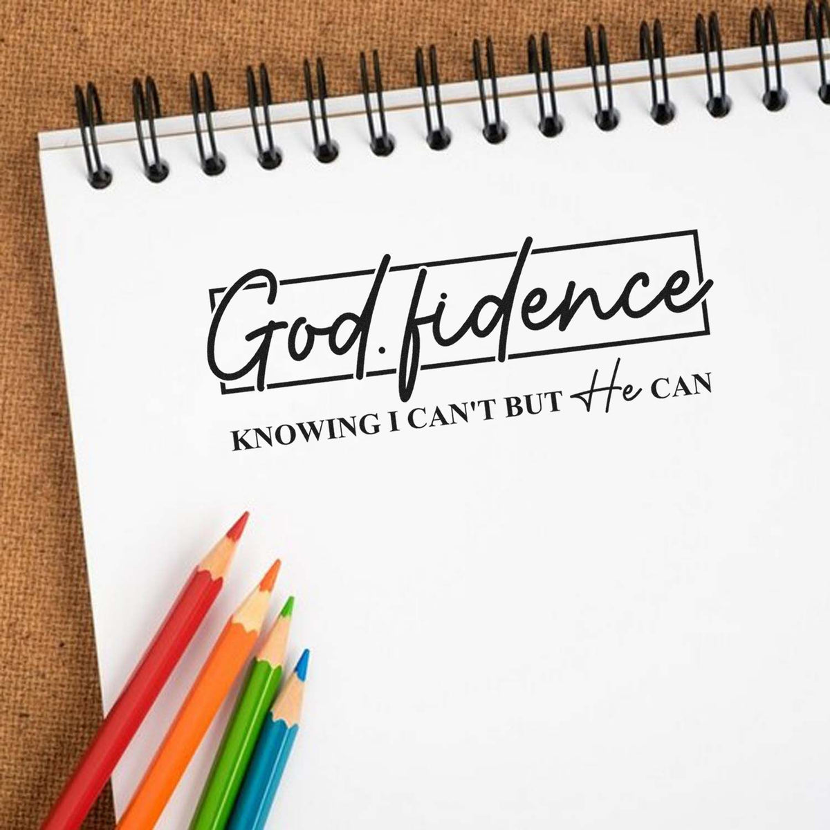 Custom stamp and seal reading God.fidence on a white spiral notebook with red, orange, green, and blue pencils.