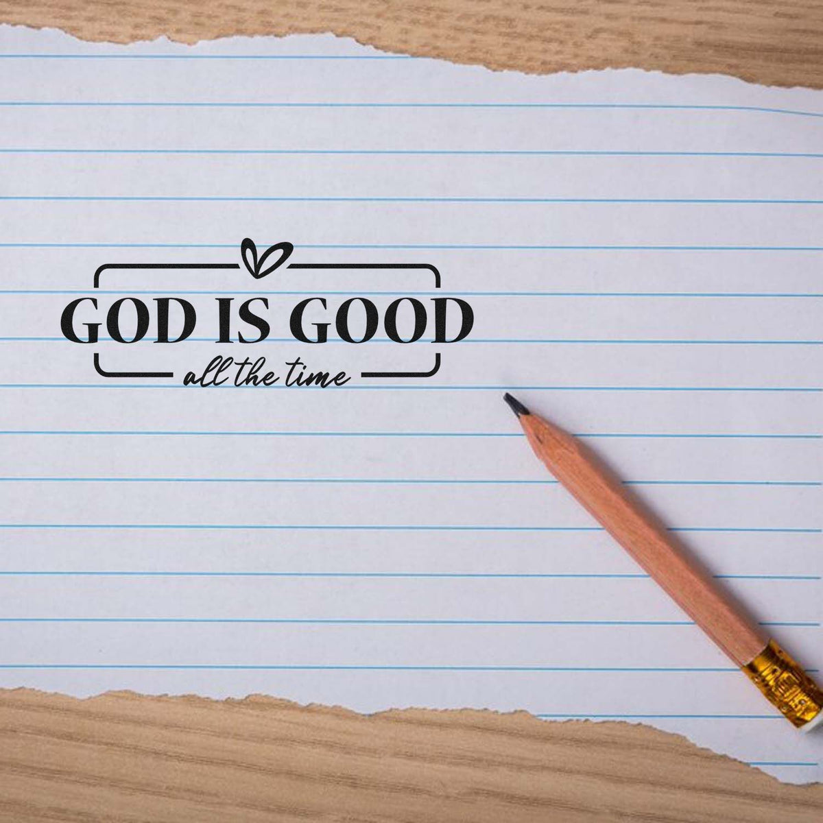 Black religious stamp seal reading God Is Good all the time on lined paper, with a pencil nearby.