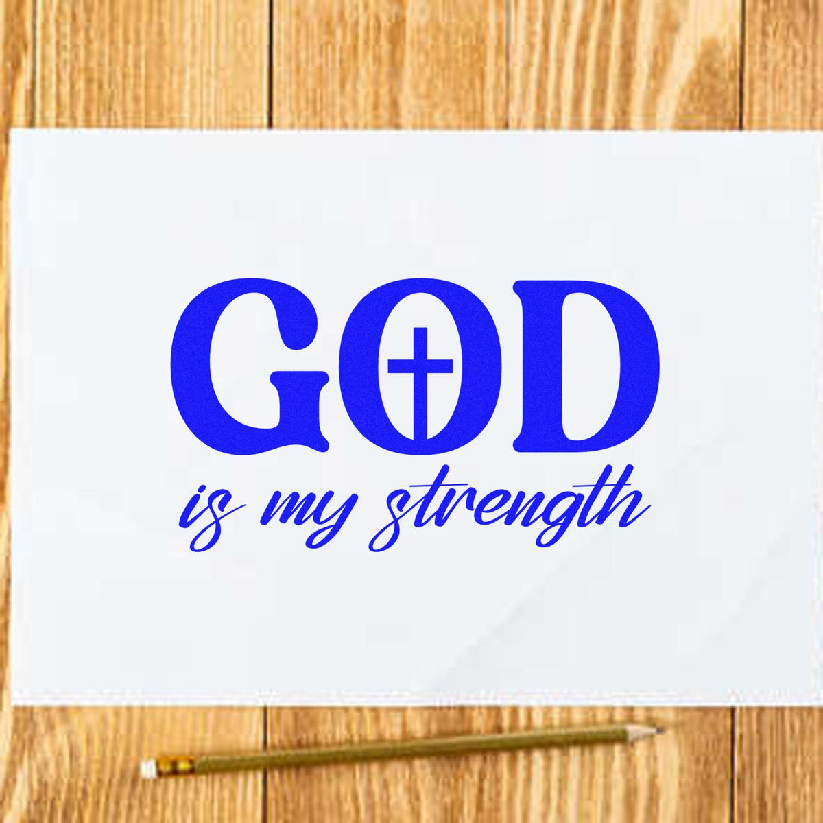 Blue custom stamp/seal design reading GOD is my strength on white paper over a wood table, with pencil.