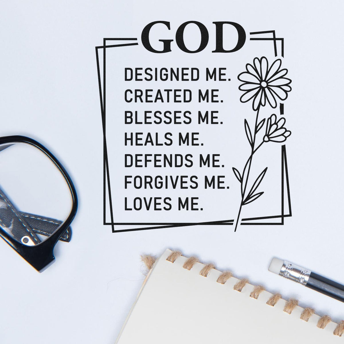 Black custom stamp design with floral border and God designed me... quote on white, beside notebook and craft tools.