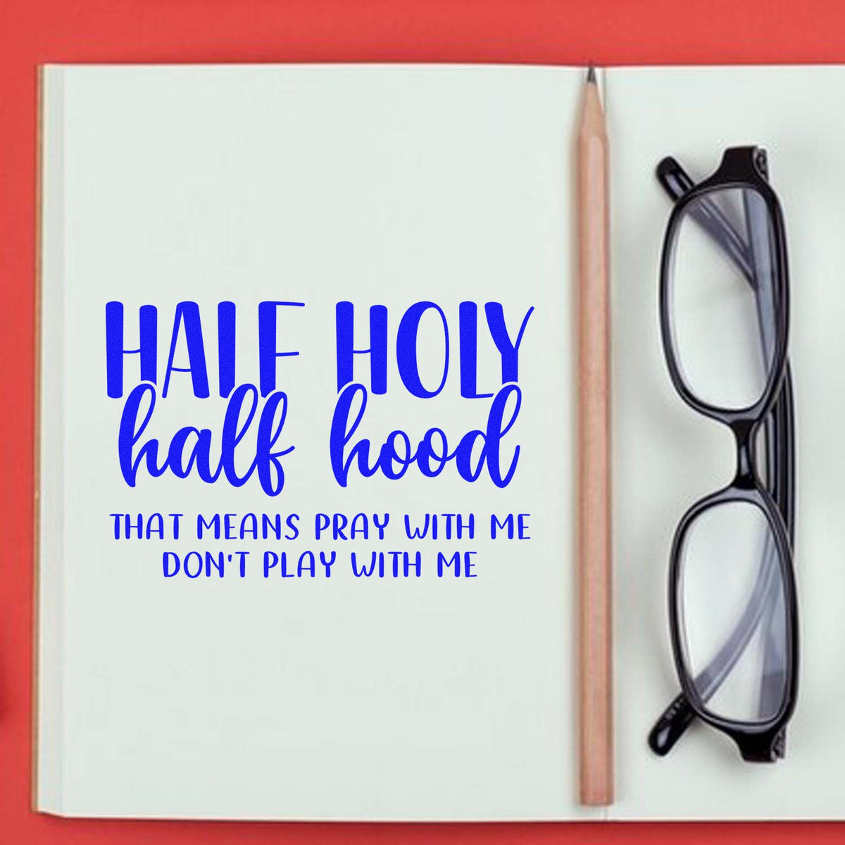 Blue Half Holy half hood stamp and seal on white notebook, with pencil and black glasses on a red background.