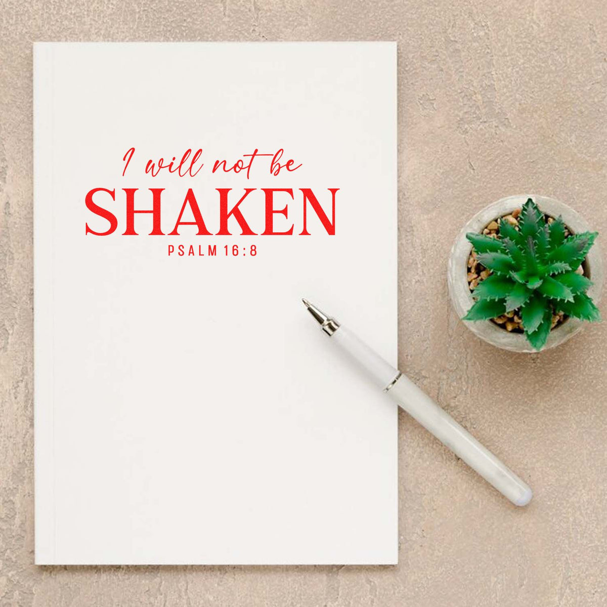 White custom stamp and seal notebook with red I will not be shaken Psalm 16:8, white pen, and green succulent on beige background.