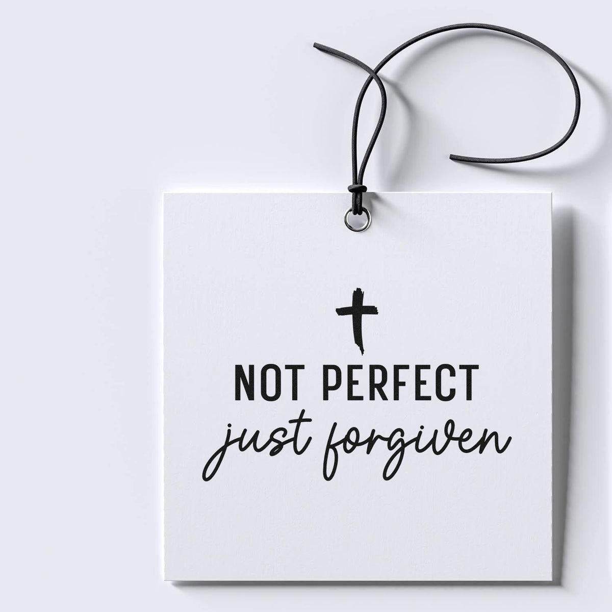 White hanging gift tag stamp and seal with black cord, printed Not perfect just forgiven in bold and script text.