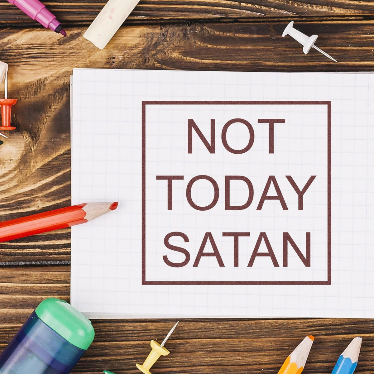 Brown NOT TODAY SATAN stamp on white grid paper, with colorful pencils and seal/stamp supplies on rustic wood.