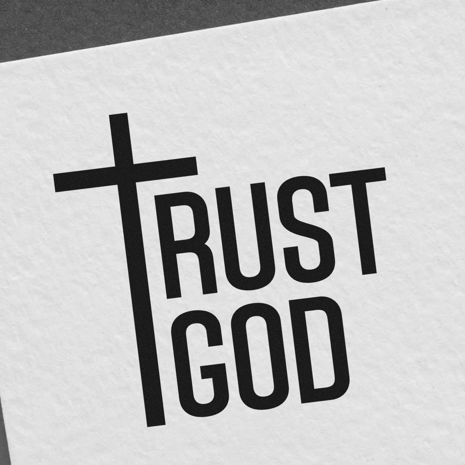 Black TRUST GOD stamp seal with cross-shaped T on white textured paper background.