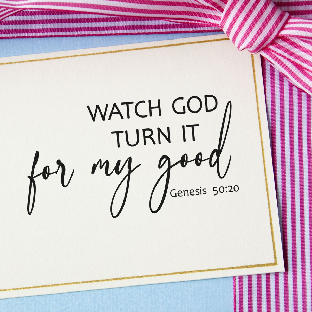 Pink striped ribbon frames a gold-bordered Bible verse stamp seal reading Watch God turn it for my good Genesis 50:20.