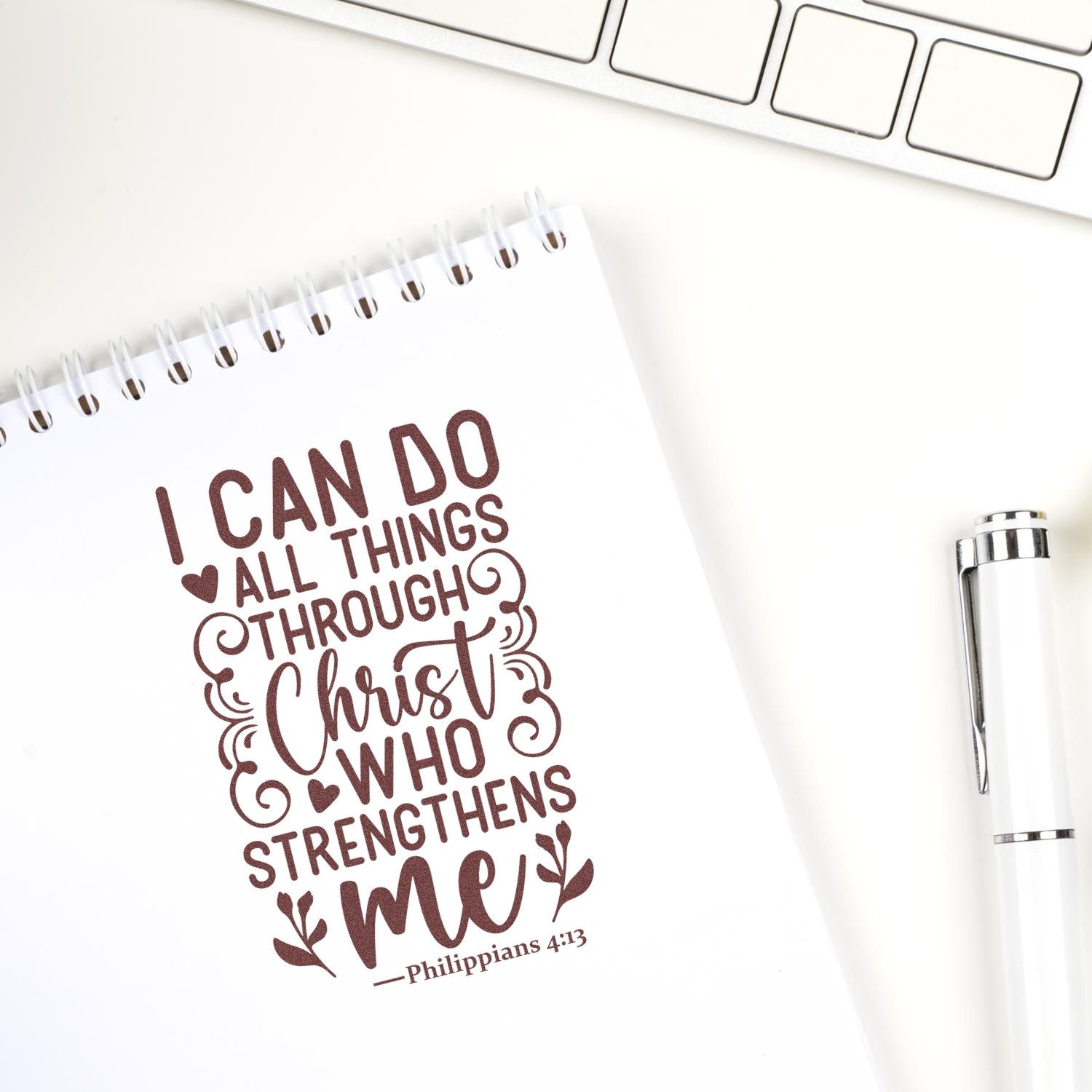 Brown custom stamp imprint on white spiral notebook reads I can do all things through Christ... beside a white pen.