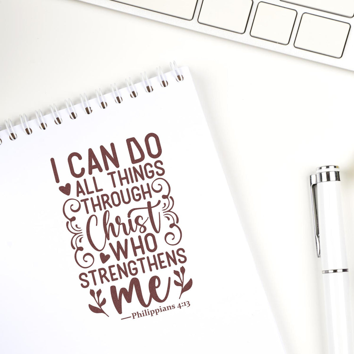 White notebook featuring a brown rubber stamp quote, with a silver pen and laptop keyboard on a clean desk.