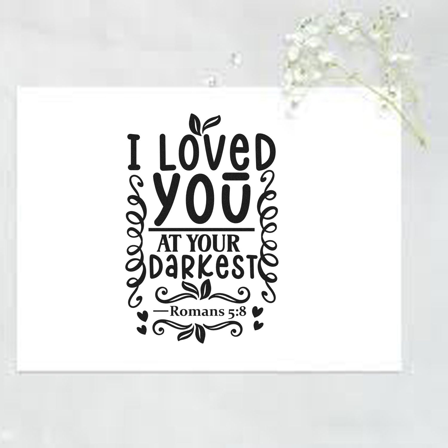 Black decorative stamp and seal design on white card reading I loved you at your darkest, Romans 5:8, with leaves and hearts.