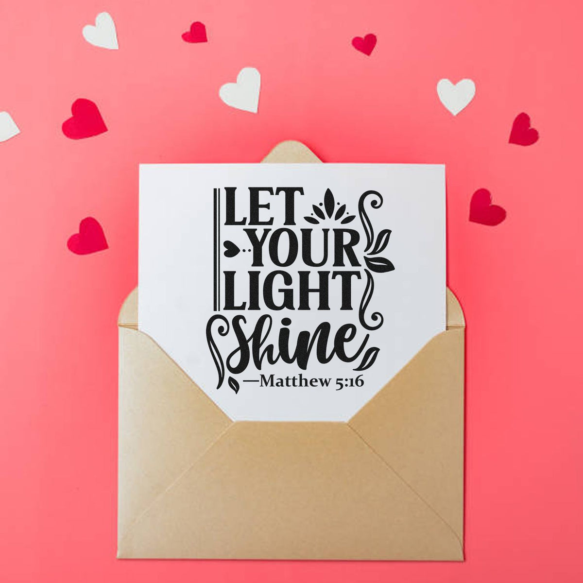 Beige envelope with white card and black Let Your Light Shine custom stamp and seal, on pink background with red and white hearts.