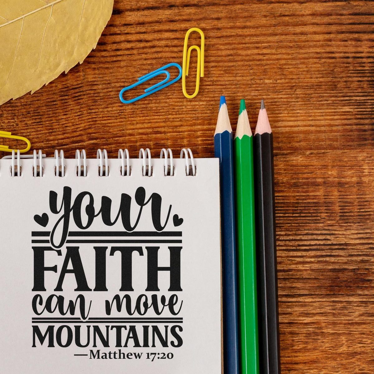 Christian faith quote notebook on wood desk with blue, green and black pencils, paper clips, and stamp and seal product mockup.