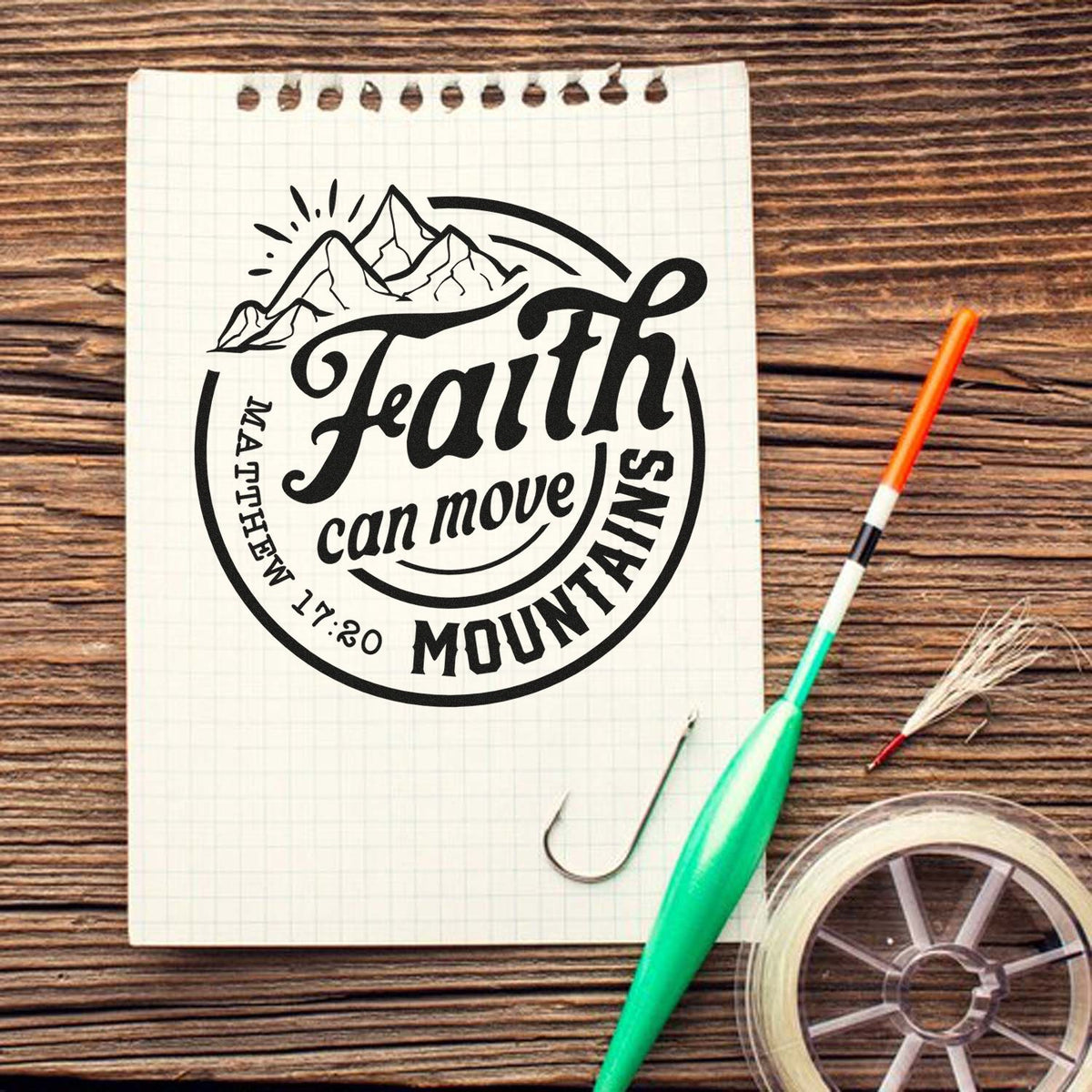 Custom black faith mountain stamp and seal on grid notebook, with green pen and twine on wood table.