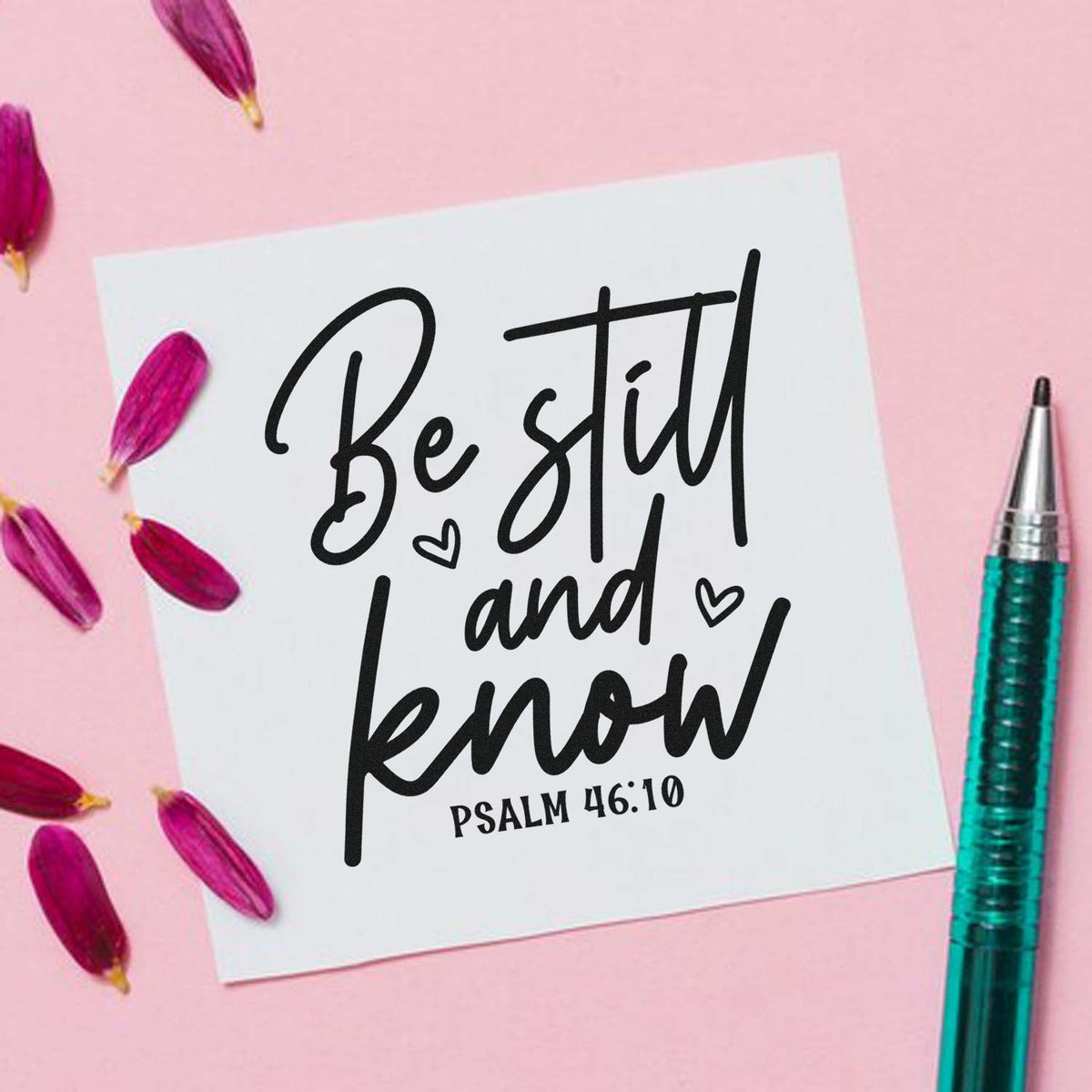 White stamp-and-seal card with black Be still and know Psalm 46:10 on pink background, with magenta petals and teal pen.
