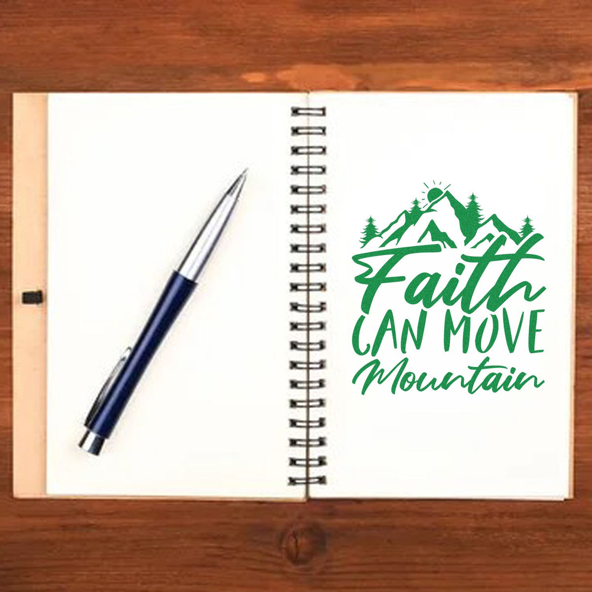 Open spiral notebook with pen and green Faith Can Move Mountain mountain stamp seal on white page.
