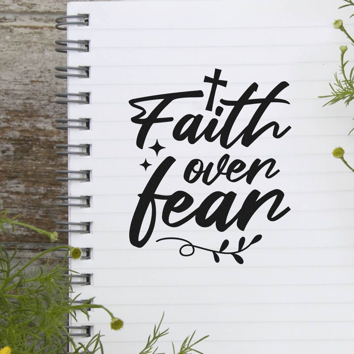 Black Faith over fear stamp seal on white spiral notebook, with star accents and leafy flourish.