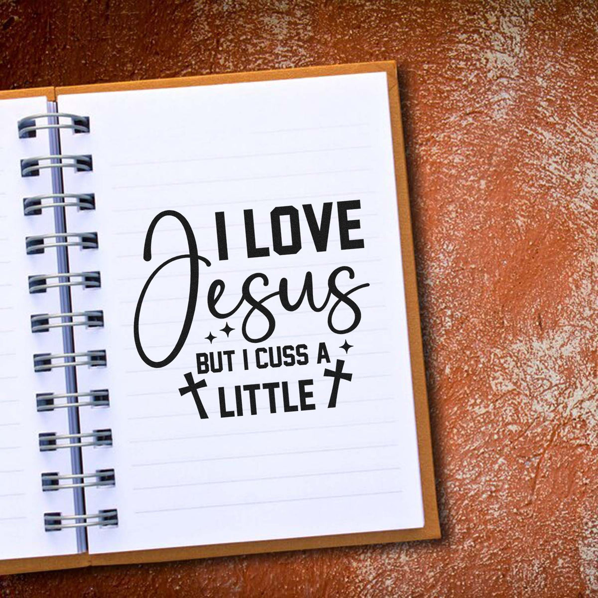 Black religious stamp and seal design on white spiral notebook page, reading I love Jesus but I cuss a little, with crosses and stars.