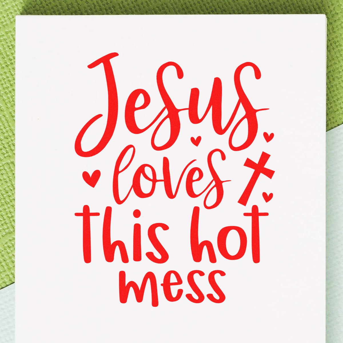 Red "Jesus loves this hot mess" stamp/seal design with hearts and a cross on a white card, on a green background