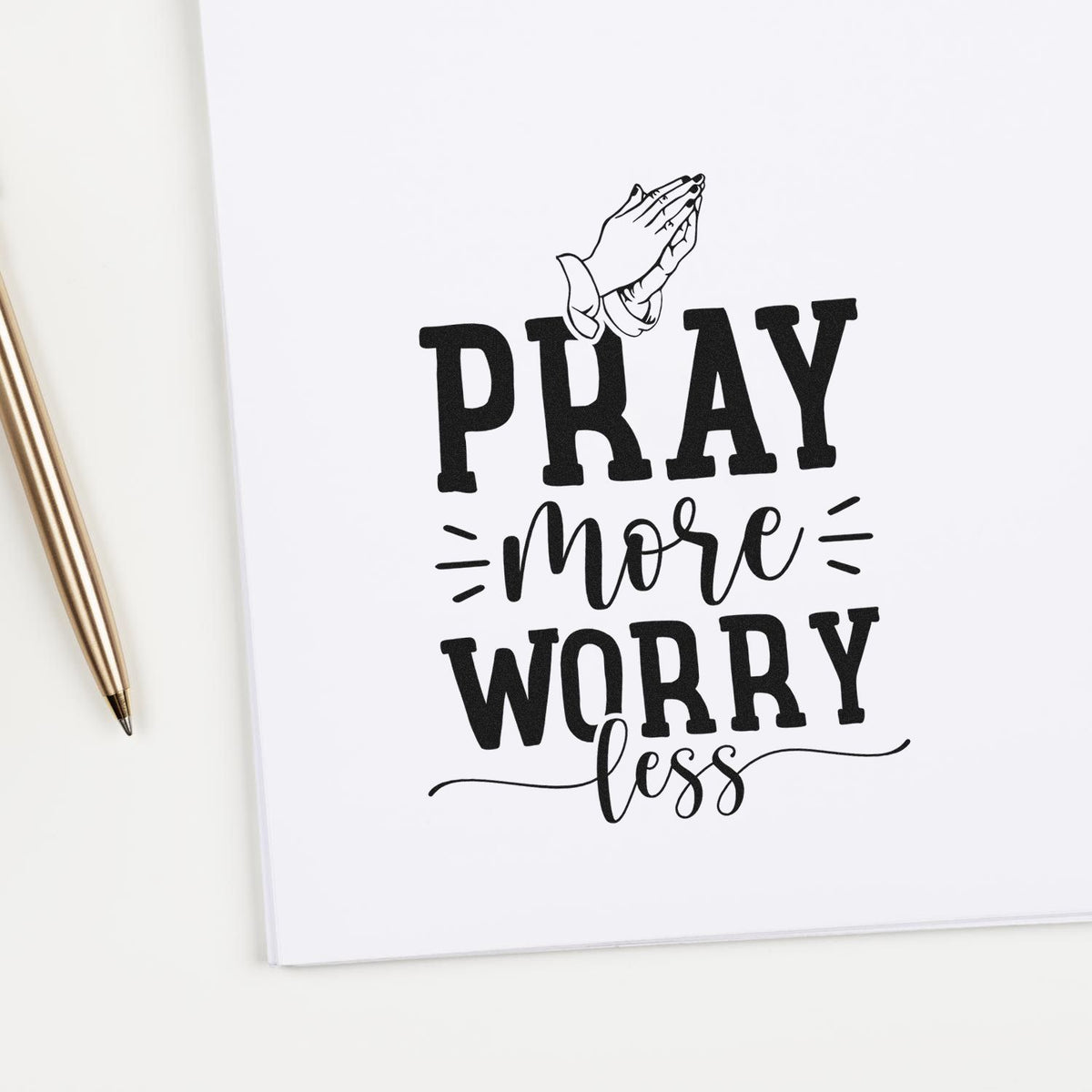 Black prayer stamp design on white paper, reading Pray more worry less, with praying hands and a gold pen.