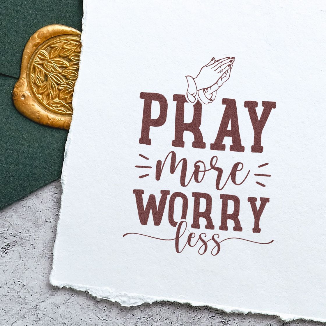 White stamped card with maroon Pray more worry less and praying hands, beside a gold wax seal on dark green.