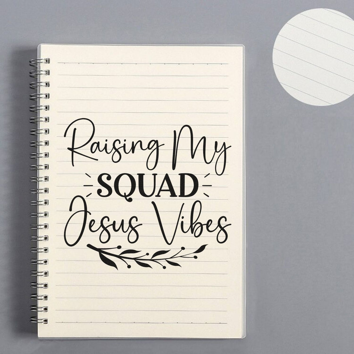 Black custom stamp and seal design on lined spiral notebook reading Raising My Squad Jesus Vibes with leaf accent.