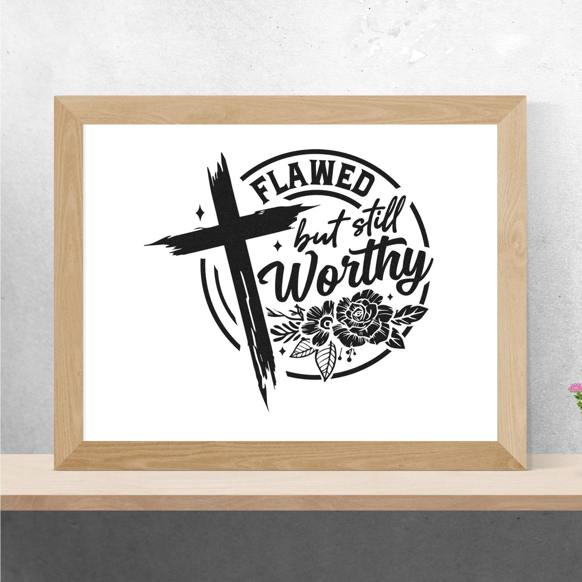 Black stamp and seal design with cross, floral details, and Flawed but still worthy in a light wood frame.